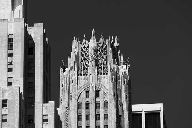 A tall, ornate building with Gothic-inspired spires and a central sculpted figure rises above surrounding structures against a dark sky.