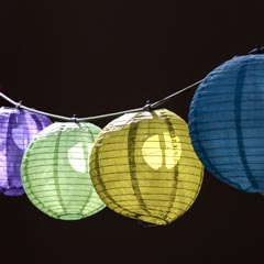 A string of paper lanterns in various colors hangs from a wire against a dark brown background.