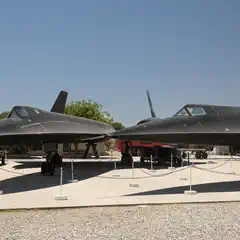 Two black stealth aircraft are on display outdoors, surrounded by a rope barrier.