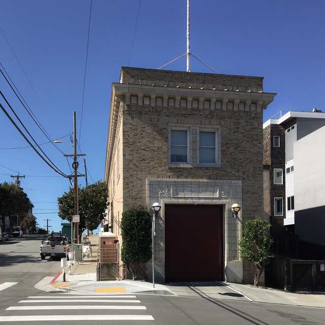 A two-story brick building with a red garage door stands on a street corner.