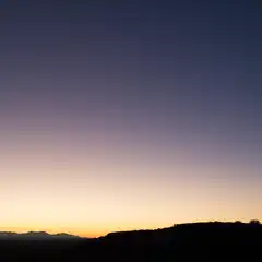 A sunset over a desert landscape features a gradient of colors in the sky, transitioning from yellow to purple and blue hues.