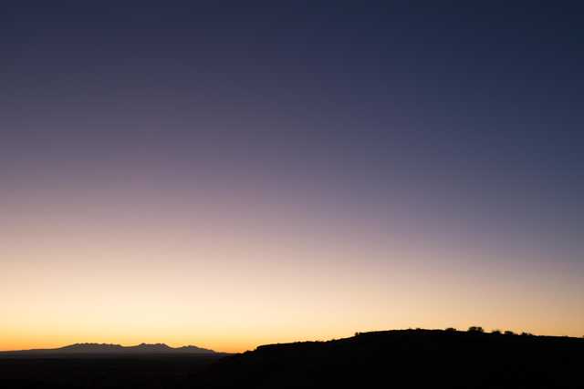 A sunset over a desert landscape features a gradient of colors in the sky, transitioning from yellow to purple and blue hues.