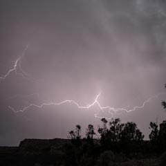 A dramatic lightning bolt illuminates a dark, stormy sky over a silhouette of trees and a rocky landscape.