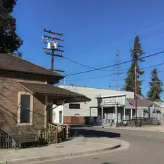 A small town street scene featuring an old-fashioned gas station and a wooden building with a porch.