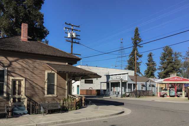 A small town street scene featuring an old-fashioned gas station and a wooden building with a porch.