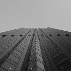 A skyscraper with a glass facade and numerous windows rises into an overcast sky.