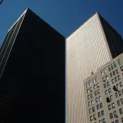 Two tall buildings are visible from below, with one building on the left having a dark facade and the other on the right featuring a light-colored facade.