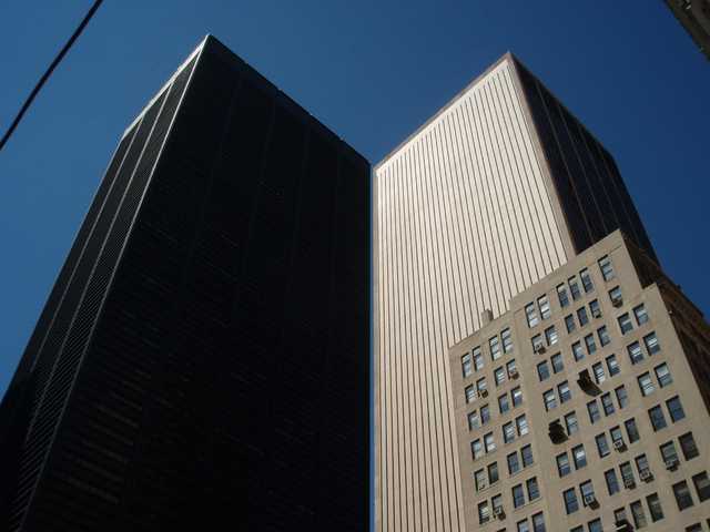 Two tall buildings are visible from below, with one building on the left having a dark facade and the other on the right featuring a light-colored facade.