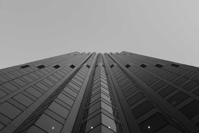 A skyscraper with a glass facade and numerous windows rises into an overcast sky.