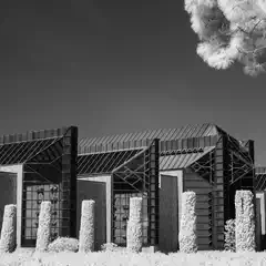 A long, low building with a repeating pattern of vertical supports and glass panels extends across the frame, and trimmed hedges line the front.