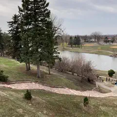 A path leads down to a lake, lined with trees and grassy areas, where several people are gathered near water's edge.
