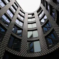 A low-angle view of a circular courtyard enclosed by a modern building with a black and white checkered facade and curved windows.