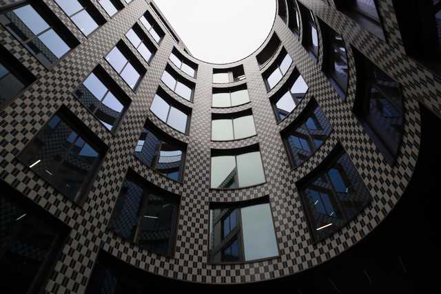 A low-angle view of a circular courtyard enclosed by a modern building with a black and white checkered facade and curved windows.