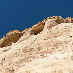 A large sandstone rock face is visible from below, with a deep blue sky above.