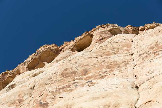 A large sandstone rock face is visible from below, with a deep blue sky above.