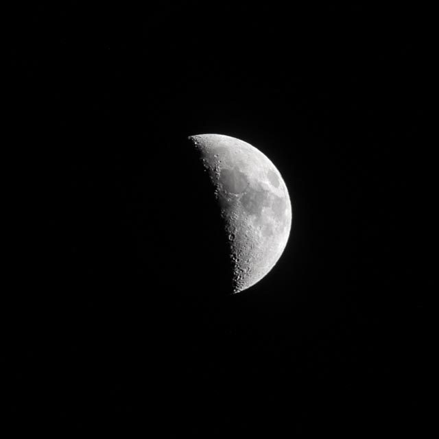An illuminated half-moon with craters and ridges is visible against a black background.