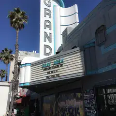 A theater marquee with a movie title and a date, set against a backdrop of palm trees under a clear blue sky.
