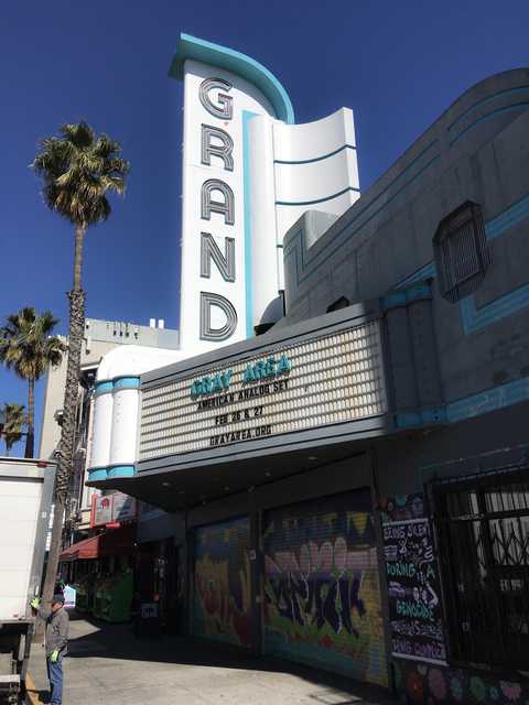 A theater marquee with a movie title and a date, set against a backdrop of palm trees under a clear blue sky.