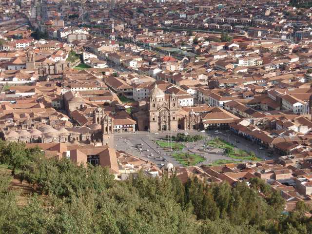 A cityscape with a large plaza surrounded by historic buildings featuring red-tiled roofs, viewed from an elevated perspective.