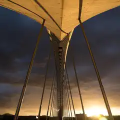 A cable-stayed bridge is silhouetted against a dramatic sunset sky.