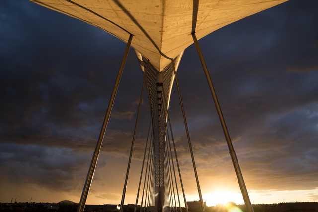 A cable-stayed bridge is silhouetted against a dramatic sunset sky.