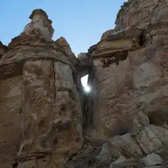 A large rock formation with a hole through the center, allowing sunlight to shine through from behind.