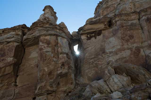A large rock formation with a hole through the center, allowing sunlight to shine through from behind.