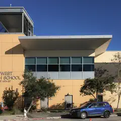 A large building with a flat roof and many windows, labeled "MetWest High School", under a clear blue sky.