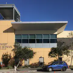 A large building with a flat roof and many windows, labeled "MetWest High School", under a clear blue sky.