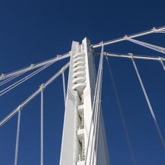 A tall, white suspension bridge with multiple cables supporting it, against a clear blue sky.