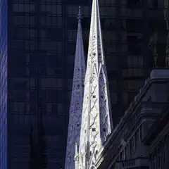 Two ornate Gothic spires rise against the dark glass facade of a modern skyscraper.