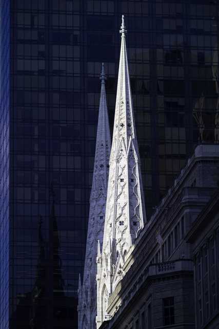 Two ornate Gothic spires rise against the dark glass facade of a modern skyscraper.