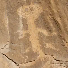 A rock face with a large, ancient petroglyph carved into it, showcasing an abstract human-like figure.