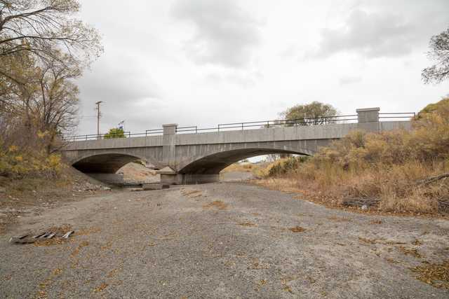 A concrete bridge over a dry riverbed with sparse vegetation and cloudy sky.