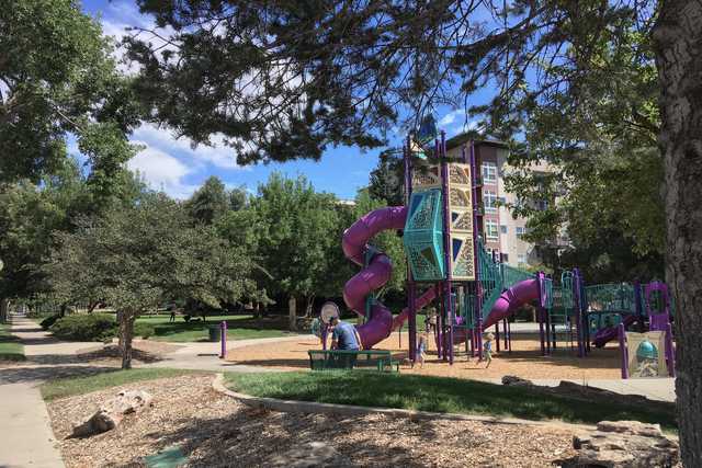 A playground with a colorful slide and climbing structures set against a backdrop of trees and a clear sky.