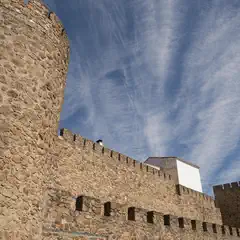 A stone castle with multiple towers and battlements, under a partly cloudy sky.