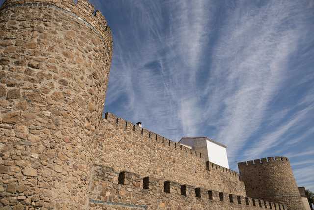 A stone castle with multiple towers and battlements, under a partly cloudy sky.