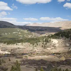 A mountainous landscape under a partly cloudy sky, with patches of greenery and water bodies interspersed among rocky terrain.