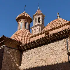 An old stone building featuring two domes topped with red clay tiles and ornate bell towers is set against a clear blue sky.