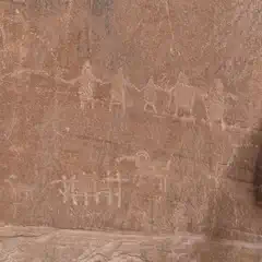 A sandstone wall contains several petroglyphs depicting human-like figures and animal shapes.
