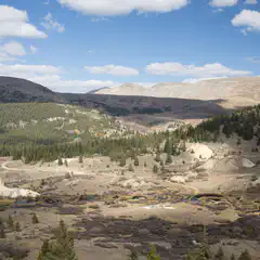 A mountainous landscape under a partly cloudy sky, with patches of greenery and water bodies interspersed among rocky terrain.