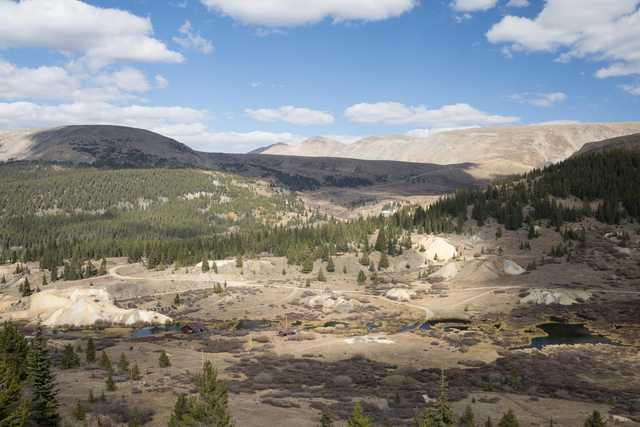 A mountainous landscape under a partly cloudy sky, with patches of greenery and water bodies interspersed among rocky terrain.