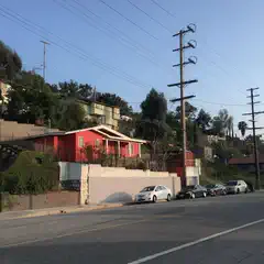 An urban street is lined with houses and cars, set against a backdrop of trees and power lines.