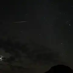 A shooting star streaks across a dark sky, leaving a trail of light behind it.