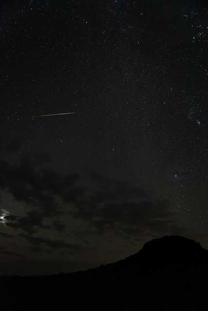 A shooting star streaks across a dark sky, leaving a trail of light behind it.