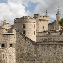 A stone fortress with crenellated walls, round and square towers, arched windows, and a flag flying atop a central spire.