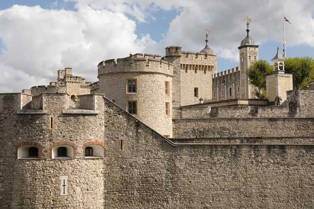 A stone fortress with crenellated walls, round and square towers, arched windows, and a flag flying atop a central spire.