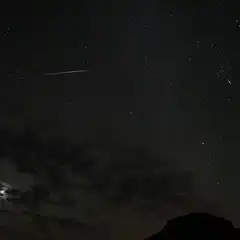 A shooting star streaks across a dark sky, leaving a trail of light behind it.