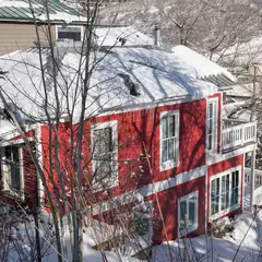 A red and white two-story house covered in snow, with bare trees around it.
