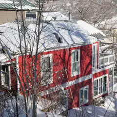A red and white two-story house covered in snow, with bare trees around it.